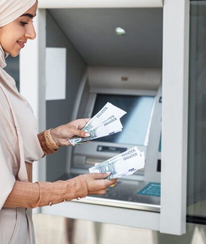 Debit and credit, money withdrawal, salary, money transfer, currency transfer outdoor. Business and work. Smiling young islamic lady in hijab counts dollars near atm machine in city, copy space