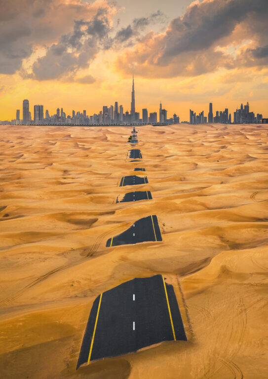 Aerial view of Dubai Downtown skyline with half desert sand road, United Arab Emirates or UAE. Financial district and business area in smart urban city. Skyscraper and high-rise buildings at sunset.